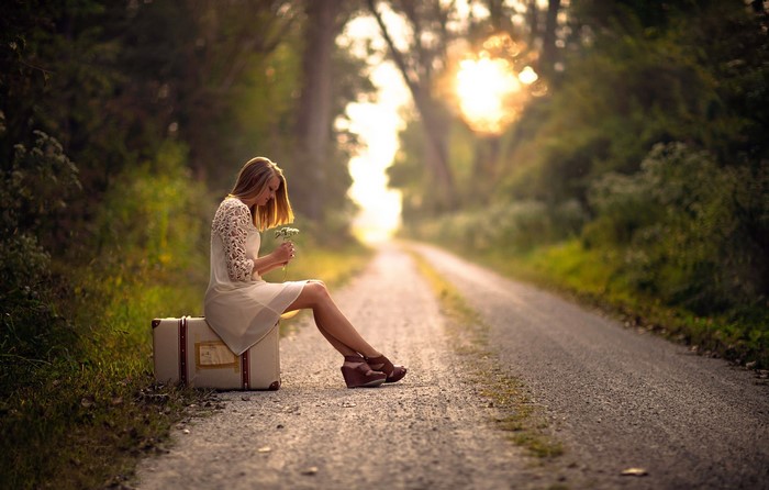 Woman sitting on a suitcase on a road