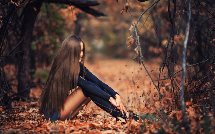 Woman with long brown hair sitting in a fall forest