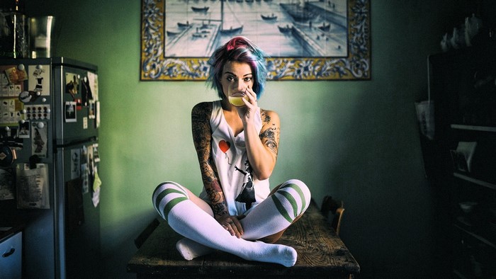 Woman with tattoos and dyed hair drinking from a glass