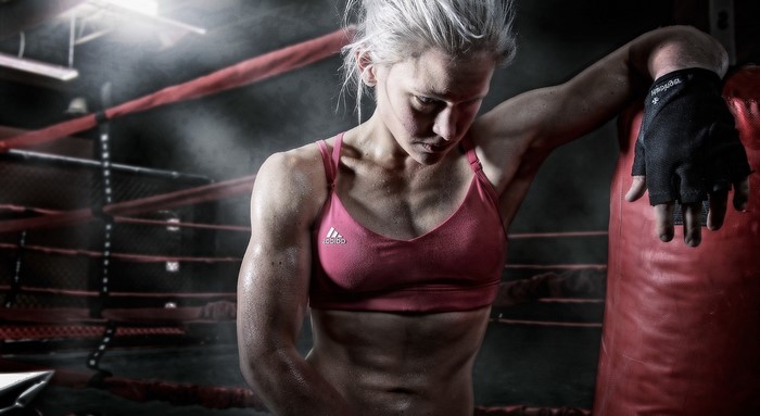 Female boxer leaning on punching bag in ring