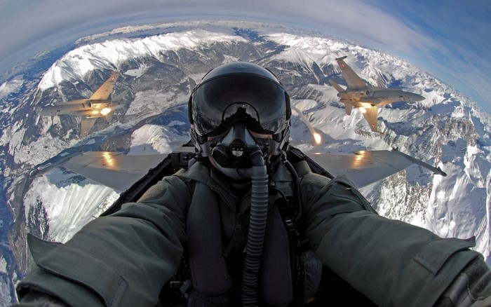 Pilot in fighter jet flying over snowy mountains with other jets