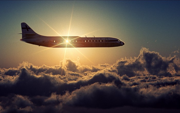 Airplane flying through clouds at sunset with lens flare