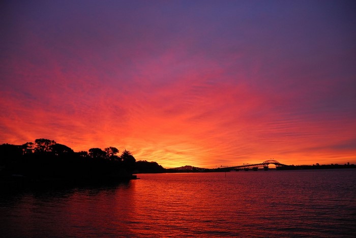 Sunset over water with bridge and trees