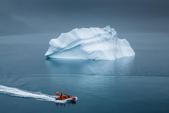 Orange boat near a large iceberg in the Arctic sea