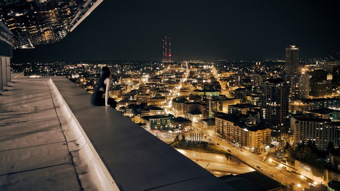 Woman sitting on a rooftop overlooking a city at night