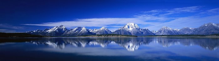 Snow-capped mountains reflected in a lake under a blue sky