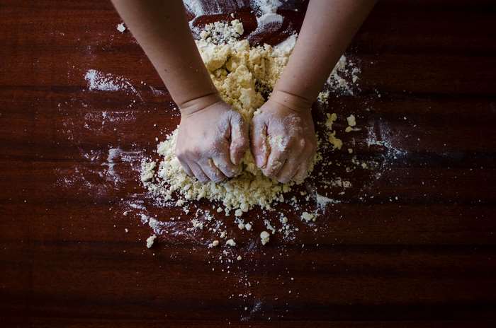 Hands kneading dough with flour on a wooden table