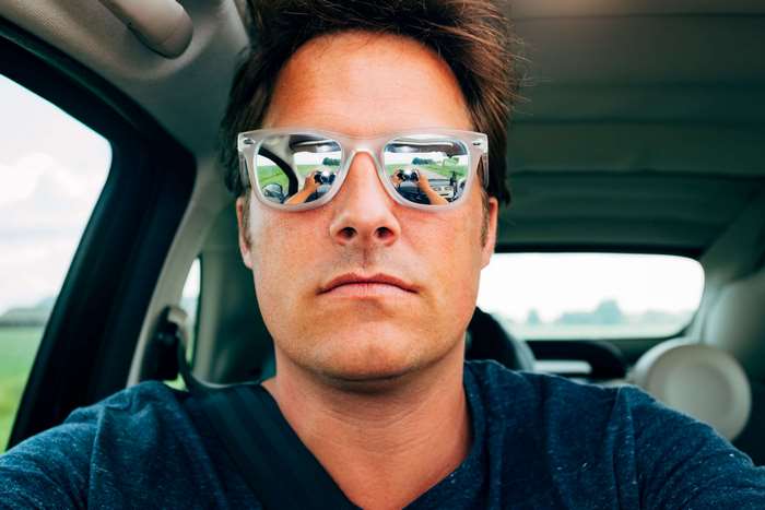 Man wearing sunglasses taking a selfie in a car