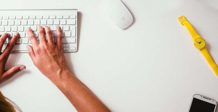 Hands typing on a keyboard with a watch and phone