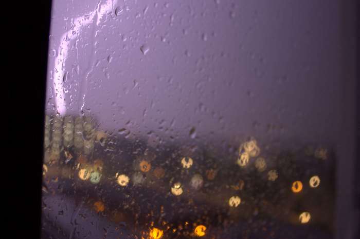 Rainy night window with city lights and lightning