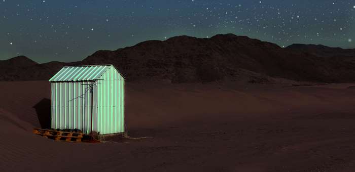 Small green corrugated metal shed in desert at night