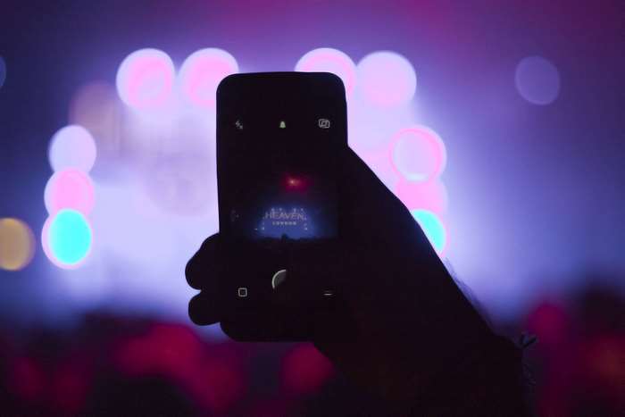 Hand holding smartphone recording a concert with bokeh lights