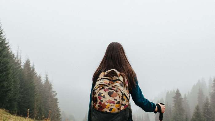 Woman with backpack hiking in foggy forest
