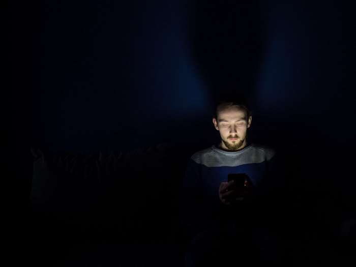 Man illuminated by smartphone screen in dark room
