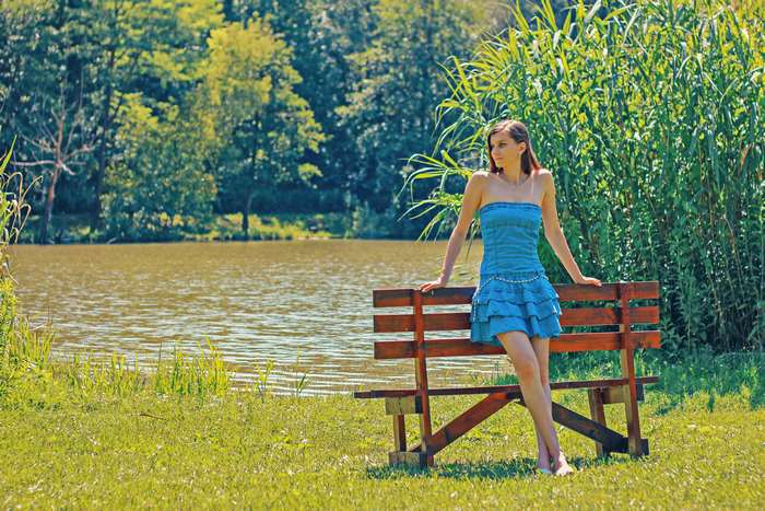 Woman in blue dress on bench by lake