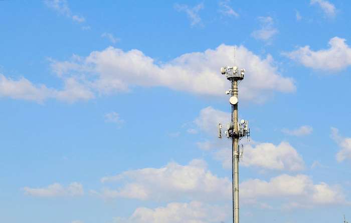 Cell tower with antennas against a blue sky with clouds