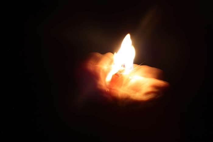 Hand holding a lighter with flames in darkness