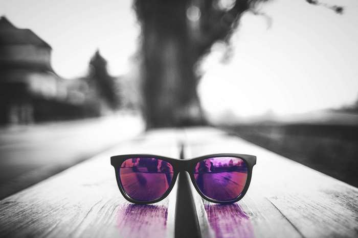 Black and white sunglasses with pink lenses on a wooden bench