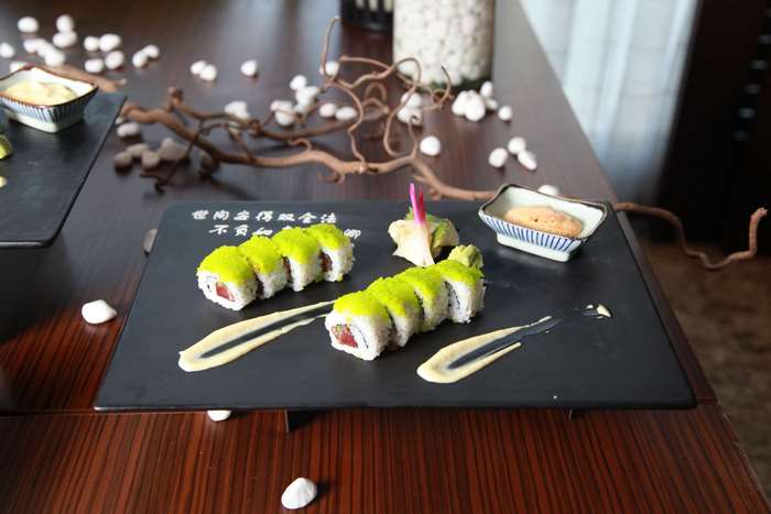 Sushi with green roe and dipping sauce on black plate