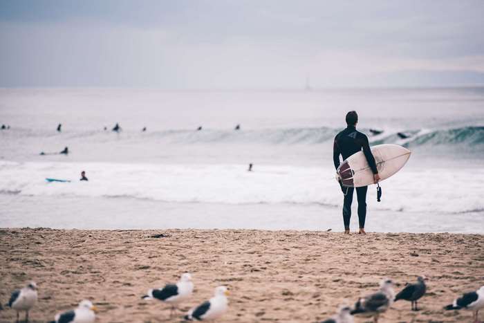 Surfer with surfboard on beach with seagulls and ocean
