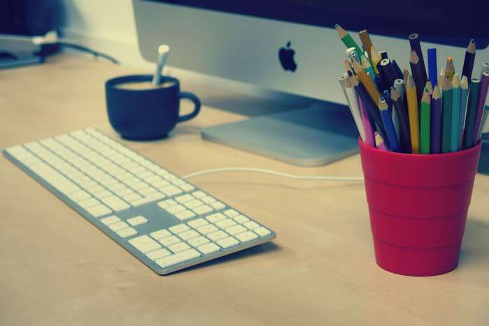 Apple computer with keyboard, coffee cup, and pencils