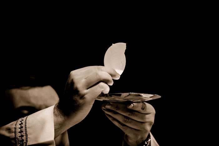Priest holding communion wafer over chalice