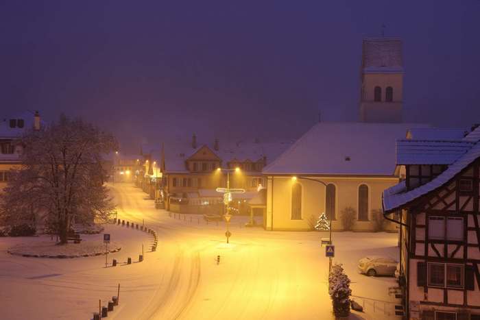 Snowy village street at night with church tower