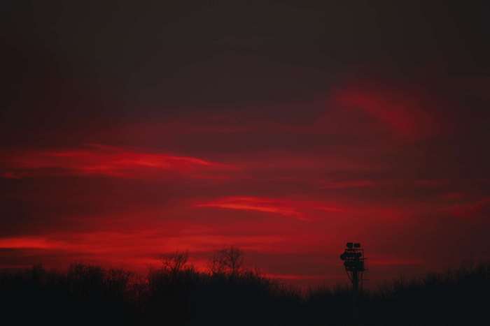 Dark red sunset over silhouetted trees and a tower