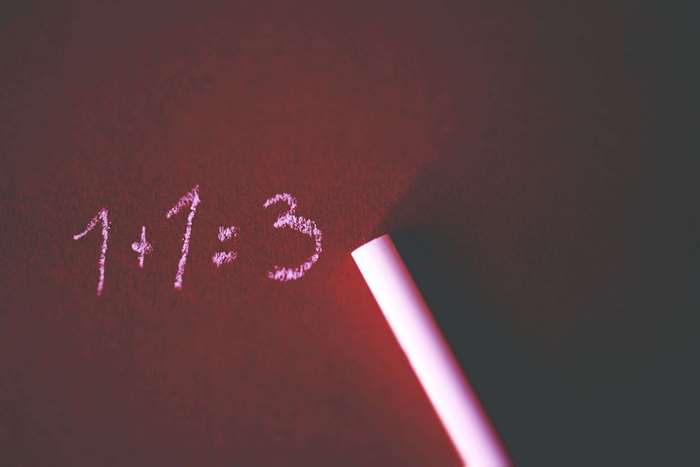 Math equation 1+1=3 written in chalk on a dark board