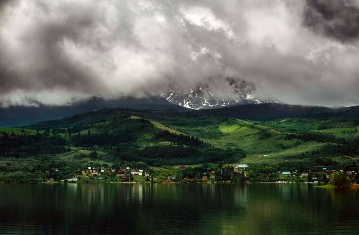 Lake with Mountains and Village Under Cloudy Sky
