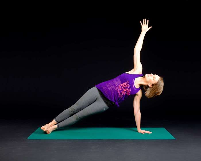 Woman performing side plank yoga pose on a mat