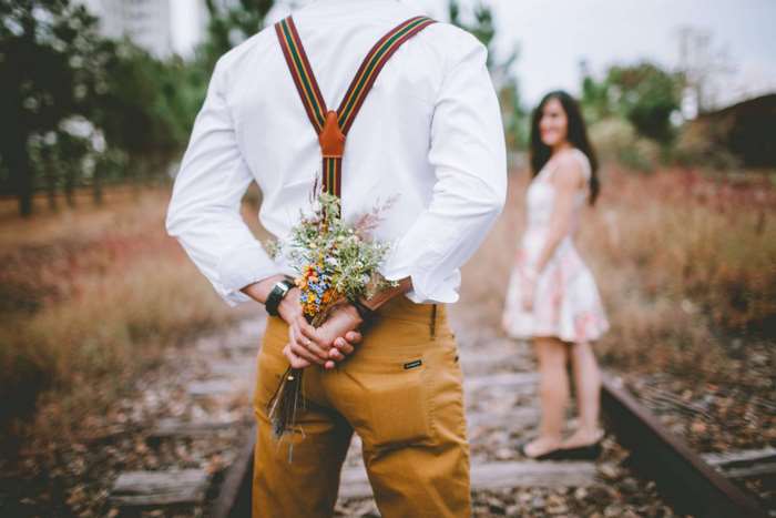 Man hiding flowers behind his back for a woman