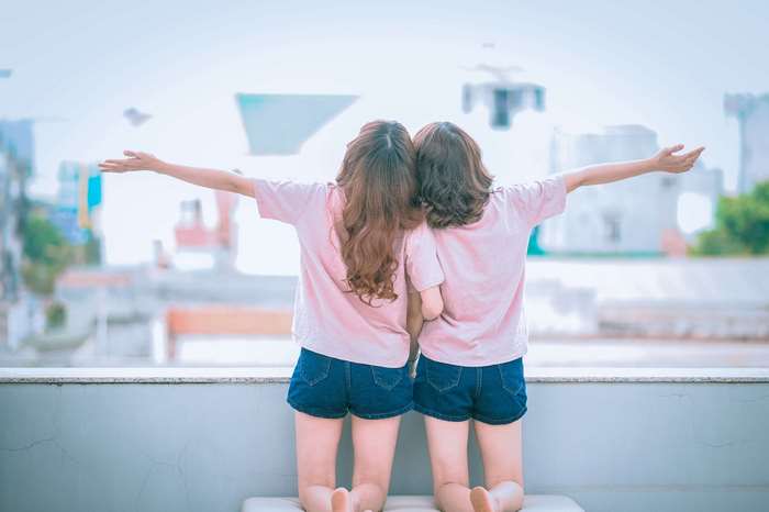 Two young women in pink shirts and denim shorts with arms outstretched