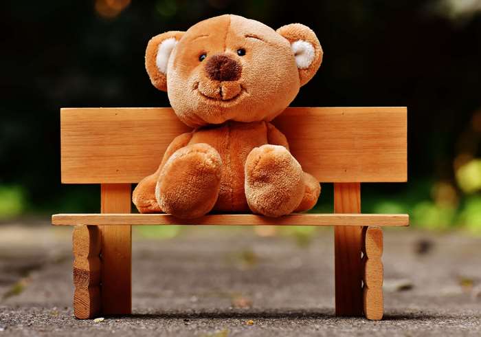 A teddy bear sits on a wooden bench