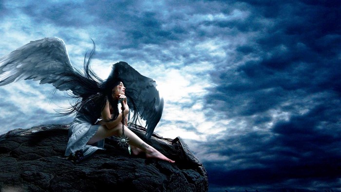 Angel with wings sitting on rocks under a cloudy sky