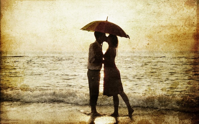 Couple kissing under umbrella on beach at sunset