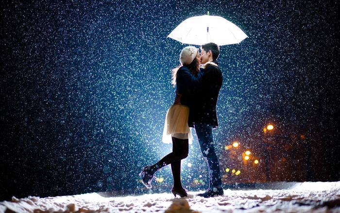 Couple kissing in the snow under an umbrella