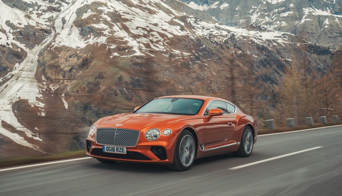 Orange Bentley Continental GT driving on a mountain road