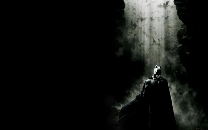 Batman standing in a cave with bats flying