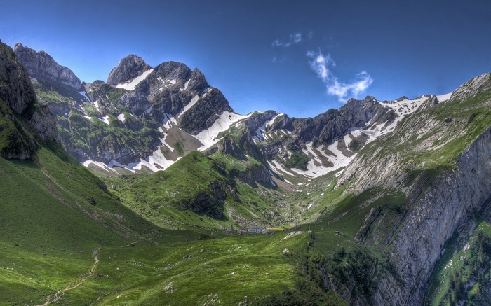 Green mountain valley with snow-capped peaks and a small village