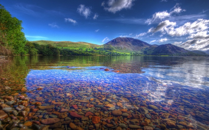 Clear lake water with pebbles and mountains in the background