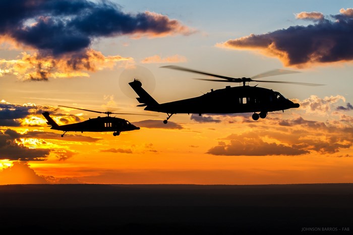 Two Sikorsky UH-60 Black Hawk helicopters flying at sunset