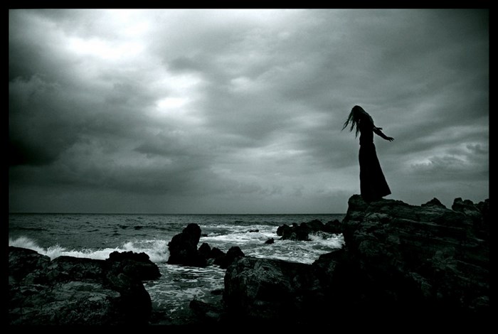 Gothic girl on rocky shore under stormy clouds