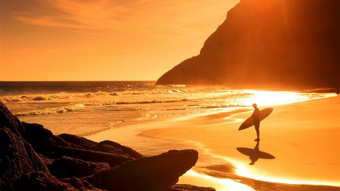 Surfer walking on beach at sunset