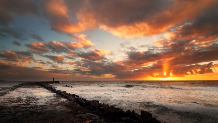 Sunset over the ocean with a pier and lighthouse