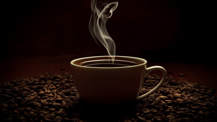 Steaming cup of coffee surrounded by coffee beans