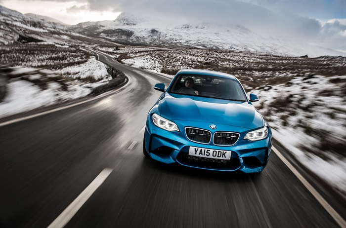 Blue BMW M2 driving on a snowy mountain road