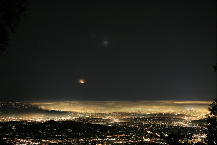 Lunar eclipse over a misty city at night with Venus and Jupiter