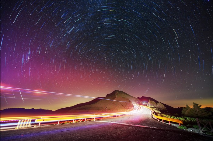 Star trails over a mountain road at night