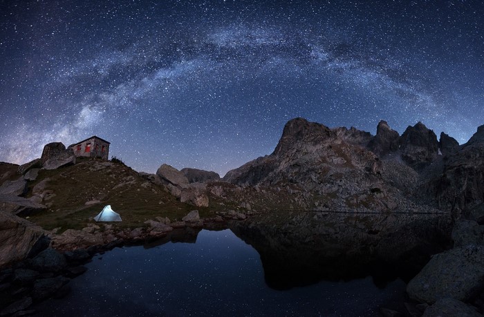 Tent and cabin under the Milky Way by a mountain lake